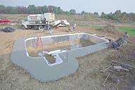 A concrete walkway is poured around the perimeter of the pool.